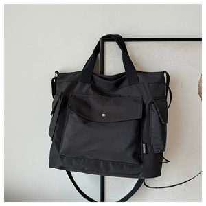 Detail view of black nylon tote bag showing front flap pocket and side pocket structure