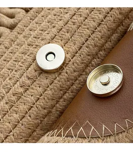 Macro detail of silver magnetic clasp and brown leather flap on straw woven handbag