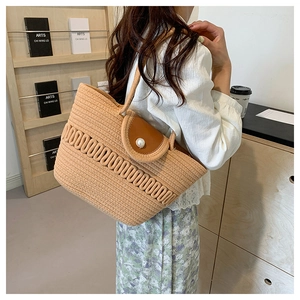 Detail of woven beach tote featuring a brown leather flap and a large pearl ornament