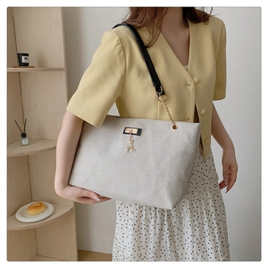 Detail of canvas tote bag featuring a gold deer charm and leather chain shoulder strap