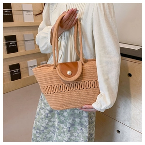 Detail of hand-woven straw bag featuring a brown leather flap and white pearl buckle