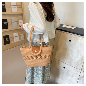 Detail of woven straw handbag with brown leather flap and pearl button on model