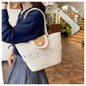 Detail of a woven straw tote bag featuring a pearl clasp and brown leather flap detail