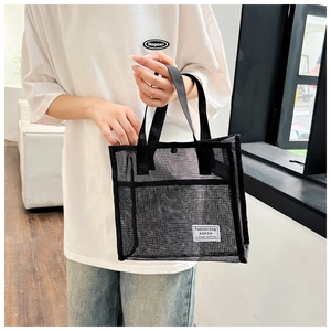 Detail of black mesh tote bag with white ACKCA label held by model in casual setting