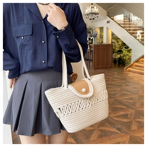 Detail of woven straw handbag featuring brown leather flap and large pearl closure