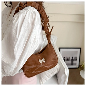 Detail of a brown shoulder bag featuring pleated strap and silver butterfly accessory