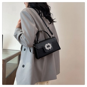 Modèle portant un sac à main en cuir noir avec boucle en cristal et fine bandoulière