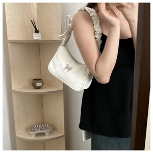 Close-up of white baguette bag with silver butterfly buckle and ruched strap detail