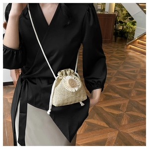 Detail of straw bucket bag with white daisy flower and drawstring strap on model