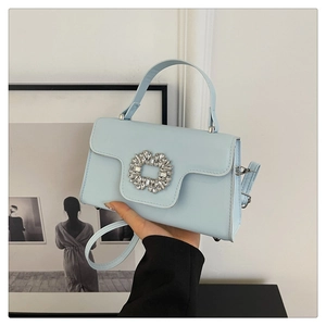 Détail du sac bandoulière bleu clair avec boucle en cristal tenu à la main pour l'échelle
