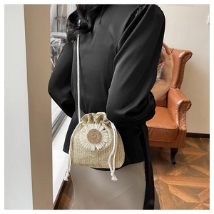 Detail of a straw bucket bag with 3D daisy flowers worn crossbody in a warm room