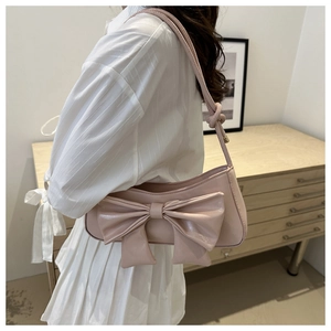 Close-up of pink glossy leather shoulder bag with oversized bow detail on the side
