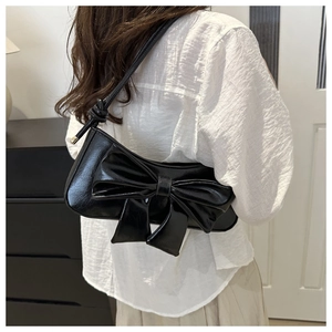 Detail of a black glossy PU shoulder bag featuring a large decorative 3D bow design