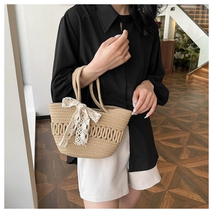 Détail du sac seau en paille tissé avec nœud en dentelle blanche et anse ronde