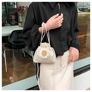 Detail of cream woven bucket bag featuring sunflower embroidery and drawstring closure