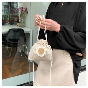 Detail of hand-woven straw bucket bag featuring a large white daisy and drawstring closure