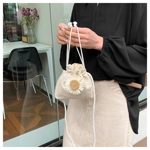Detailed close-up of a beige straw bucket bag with floral daisy decoration and drawstring
