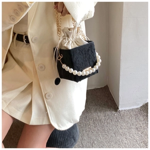 Detail of black pleated bucket bag featuring elegant pearl handle and fine gold chain strap