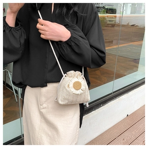 Detail of straw bucket bag featuring a white daisy flower accent and drawstring closure
