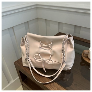Close-up of pink leather crossbody bag with decorative bow and silver chain strap