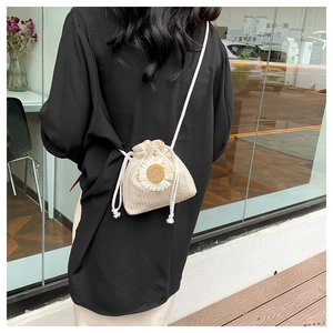 Detail of a beige straw bucket bag with daisy embroidery and drawstring closure