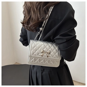 Detail of silver quilted crossbody bag with metal bow on model in black pleated skirt