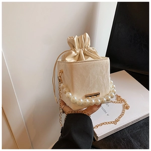 Detail of cream white bucket bag featuring pleated leather texture and pearl handle