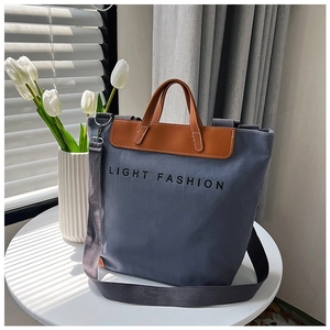 Detalle del bolso tote de lona azul con asas de cuero marrón y correa ajustable