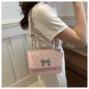 Close-up of pink quilted crossbody bag with silver bow accent and chain strap worn by model