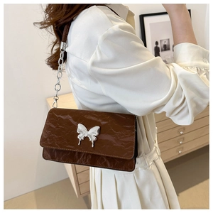 Detailed view of brown wrinkled patent leather bag with liquid silver butterfly emblem