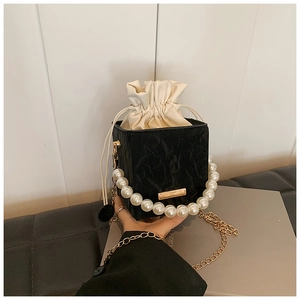 Detail of black embossed square bag featuring large pearl handle and gold chain strap