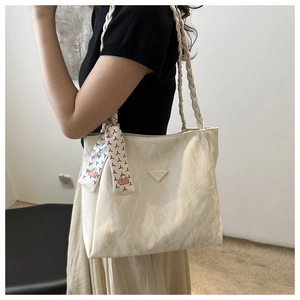 Close-up of beige tote bag with woven handles and decorative scarf on a model