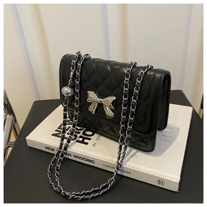 Detail of black quilted crossbody bag featuring silver bow lock and chain strap