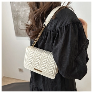 Detail of white chevron quilted shoulder bag with gold metal buckle on model