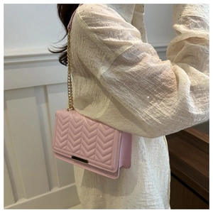 Detail of pink quilted shoulder bag with gold chain strap and metallic clasp on model