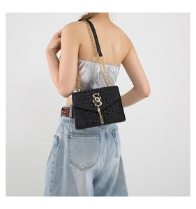 Détail du sac noir texture croco avec chaîne dorée et franges sur une tenue