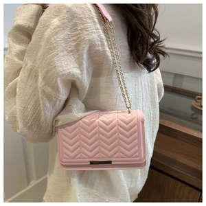 Detail of pink quilted shoulder bag with gold chain strap and V-shaped stitching pattern