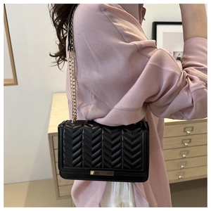 Detail of black quilted leather shoulder bag with V-pattern and gold chain strap on model