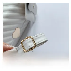 Detail of white quilted leather bag showing gold heart ornament and adjustable strap buckle