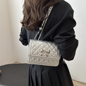 Silver quilted crossbody bag with metal bow and chain strap shown on model's shoulder