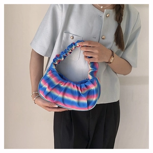 Close-up of rainbow gradient pleated cloud bag held by a model in casual attire