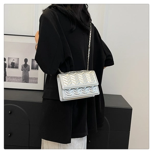 Detail of silver chevron quilted crossbody bag with gold chain strap on black blazer