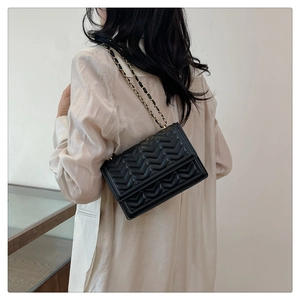 Model wearing black quilted chain bag with V-pattern stitching on white shirt