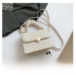 Detail of cream quilted crossbody bag with heart-shaped gold lock and ruffle handle