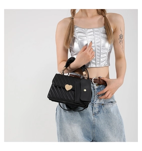 Detail of black quilted handbag featuring a gold heart lock and textured mini side pouch