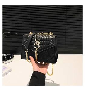 Détail d'un sac à bandoulière noir effet crocodile avec boucle S dorée et pompon chic