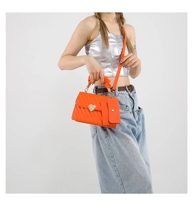 Detail of orange quilted crossbody bag with golden heart lock and mini coin purse charm