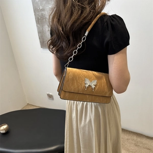 Brown PU leather shoulder bag with metallic butterfly and chain strap on a model