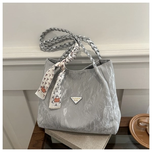 Detail of silver pleated tote bag with woven handles and decorative scarf on a book
