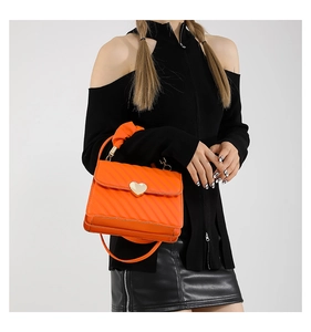 Detail of bright orange crossbody bag featuring quilted texture and gold heart-shaped lock